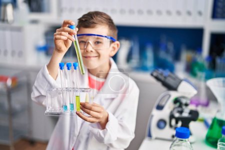 Foto de Niño rubio vistiendo uniforme científico sosteniendo tubos de ensayo en laboratorio - Imagen libre de derechos