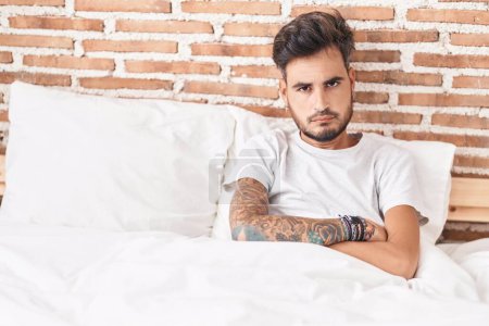 Photo for Young hispanic man sitting on bed with unhappy expression and arms crossed gesture at bedroom - Royalty Free Image