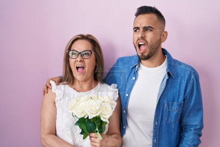 Téléchargez les photos : Mère hispanique et fils tenant ensemble un bouquet de fleurs blanches en colère et folles hurlant frustrées et furieuses, criant de colère. rage et concept agressif. - en image libre de droit