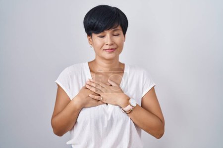 Photo for Young asian woman with short hair standing over isolated background smiling with hands on chest with closed eyes and grateful gesture on face. health concept. - Royalty Free Image