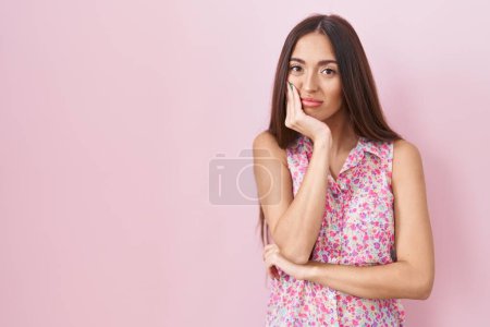 Photo for Young hispanic woman with long hair standing over pink background thinking looking tired and bored with depression problems with crossed arms. - Royalty Free Image
