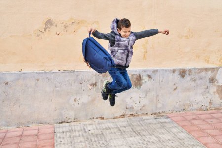 Téléchargez les photos : Enfant blond tenant un sac à dos sautant dans la rue - en image libre de droit