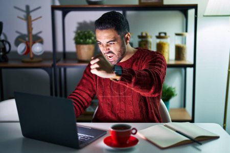 Photo for Young hispanic man with beard using computer laptop at night at home angry and mad raising fist frustrated and furious while shouting with anger. rage and aggressive concept. - Royalty Free Image
