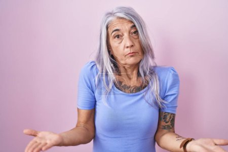 Photo for Middle age woman with tattoos standing over pink background clueless and confused with open arms, no idea concept. - Royalty Free Image