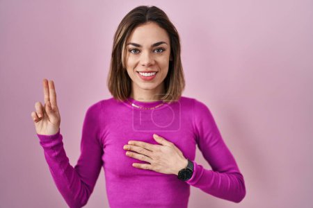 Téléchargez les photos : Hispanic woman standing over pink background smiling swearing with hand on chest and fingers up, making a loyalty promise oath - en image libre de droit