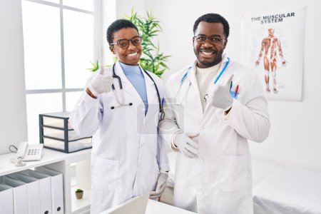 Téléchargez les photos : Jeunes médecins afro-américains travaillant à la clinique médicale souriant heureux et positif, pouce levé faire excellent et signe d'approbation - en image libre de droit