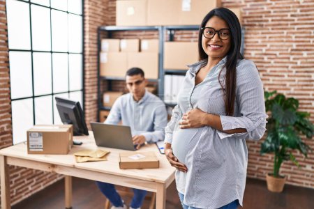 Photo for Young hispanic woman expecting a baby working at small business ecommerce looking positive and happy standing and smiling with a confident smile showing teeth - Royalty Free Image