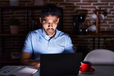Foto de Hombre hispano con barba usando laptop por la noche deprimido y preocupado por la angustia, llorando enojado y asustado. expresión triste. - Imagen libre de derechos