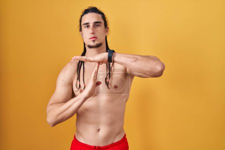 Téléchargez les photos : Homme hispanique aux cheveux longs, torse nu sur fond jaune, faisant un geste avec les mains, frustré et sérieux. - en image libre de droit