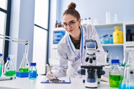 Photo for Young woman scientist writing on clipboard at laboratory - Royalty Free Image