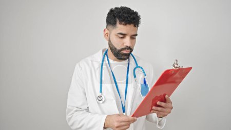 Téléchargez les photos : Jeune homme hispanique médecin lecture document sur presse-papiers sur fond blanc isolé - en image libre de droit