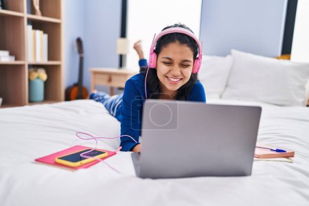 Foto de Mujer latina joven escuchando música tumbada en la cama en el dormitorio - Imagen libre de derechos
