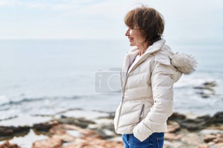 Téléchargez les photos : Femme d'âge moyen souriant confiance debout au bord de la mer - en image libre de droit