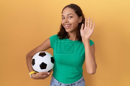 Photo for Young hispanic woman holding ball waiving saying hello happy and smiling, friendly welcome gesture - Royalty Free Image