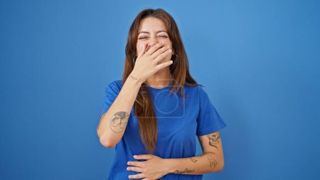 Foto de Joven hermosa mujer hispana riendo mucho cubriendo la boca con las manos sobre un fondo azul aislado - Imagen libre de derechos