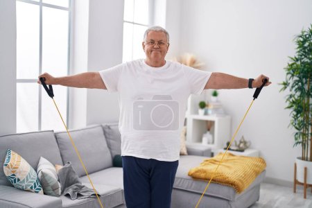 Photo for Middle age grey-haired man smiling confident using elastic band training at home - Royalty Free Image
