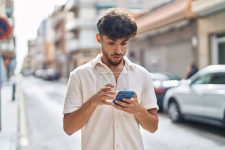 Foto de Hombre árabe joven usando teléfono inteligente con expresión sorpresa en la calle - Imagen libre de derechos