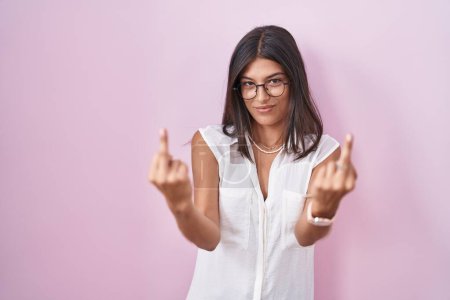 Foto de Brunette young woman standing over pink background wearing glasses showing middle finger doing fuck you bad expression, provocation and rude attitude. screaming excited - Imagen libre de derechos