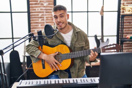 Photo for Young hispanic man musician singing song playing classical guitar at music studio - Royalty Free Image