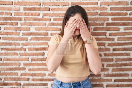 Téléchargez les photos : Jeune femme brune debout sur un mur de briques frottant les yeux pour la fatigue et les maux de tête, somnolent et l'expression fatiguée. problème de vision - en image libre de droit