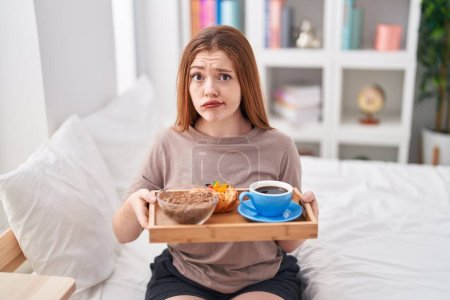 Photo for Redhead woman wearing pajama holding breakfast tray skeptic and nervous, frowning upset because of problem. negative person. - Royalty Free Image