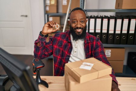 Photo for African american man working at small business ecommerce holding bitcoin looking positive and happy standing and smiling with a confident smile showing teeth - Royalty Free Image