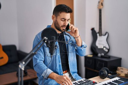 Téléchargez les photos : Jeune homme hispanique artiste souriant confiant parler sur le smartphone au studio de musique - en image libre de droit