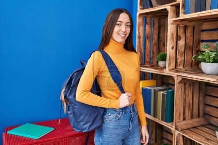 Téléchargez les photos : Jeune belle étudiante hispanique souriante portant un sac à dos confiant à la maison - en image libre de droit