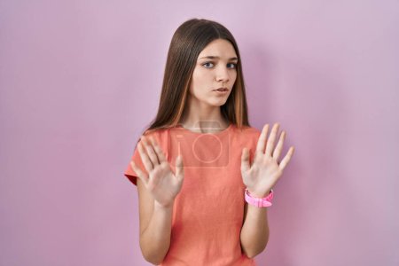 Photo for Teenager girl standing over pink background moving away hands palms showing refusal and denial with afraid and disgusting expression. stop and forbidden. - Royalty Free Image
