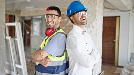 Téléchargez les photos : Deux hommes constructeur et architecte souriant confiant debout avec les bras croisés geste sur le chantier de construction - en image libre de droit