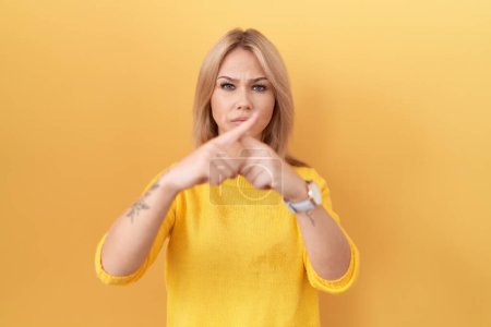 Téléchargez les photos : Jeune femme caucasienne portant un pull jaune expression de rejet croisant les doigts faisant signe négatif - en image libre de droit