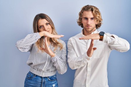 Photo for Young couple standing over blue background doing time out gesture with hands, frustrated and serious face - Royalty Free Image
