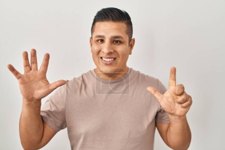 Foto de Joven hispano de pie sobre fondo blanco mostrando y señalando con los dedos número siete mientras sonríe confiado y feliz. - Imagen libre de derechos