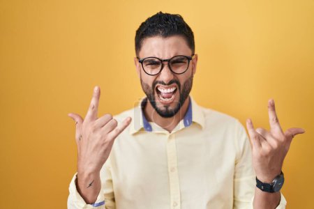 Photo for Hispanic young man wearing business clothes and glasses shouting with crazy expression doing rock symbol with hands up. music star. heavy music concept. - Royalty Free Image