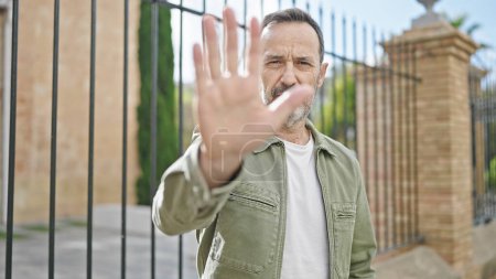Foto de Middle age man doing stop gesture with hand at street - Imagen libre de derechos