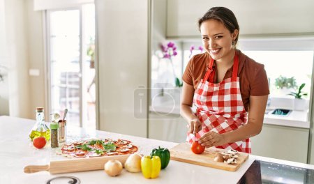 Photo for Young beautiful hispanic woman smiling confident cutting tomato at the kitchen - Royalty Free Image