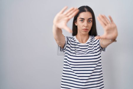 Téléchargez les photos : Jeune femme brune portant un t-shirt rayé faisant cadre en utilisant les mains, les paumes et les doigts, perspective de la caméra - en image libre de droit