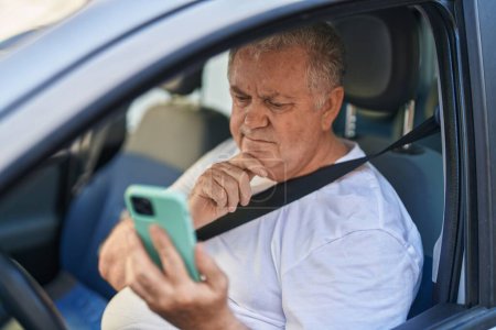 Foto de Hombre de pelo gris de mediana edad usando un teléfono inteligente sentado en el coche en la calle - Imagen libre de derechos