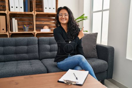 Téléchargez les photos : Jeune femme asiatique au bureau de consultation gaie avec un sourire sur le visage pointant avec la main et le doigt sur le côté avec une expression heureuse et naturelle - en image libre de droit