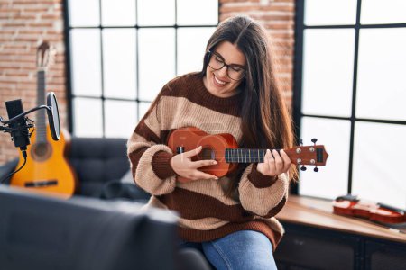 Photo for Young hispanic woman musician playing ukulele at music studio - Royalty Free Image