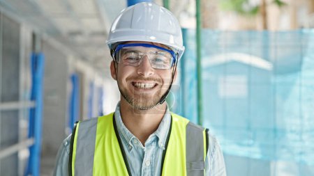 Foto de Joven hombre caucásico arquitecto sonriendo confiado de pie en el lugar de construcción - Imagen libre de derechos