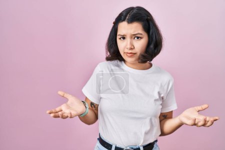Photo for Young hispanic woman wearing casual white t shirt over pink background clueless and confused with open arms, no idea concept. - Royalty Free Image