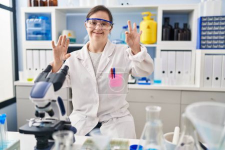 Photo for Hispanic girl with down syndrome working at scientist laboratory showing and pointing up with fingers number eight while smiling confident and happy. - Royalty Free Image