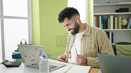 Téléchargez les photos : Jeune homme hispanique étudiant écoutant de la musique en utilisant un stylo comme batteur à l'université de la bibliothèque - en image libre de droit