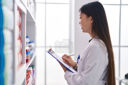 Photo for Chinese woman pharmacist writing on document at pharmacy - Royalty Free Image