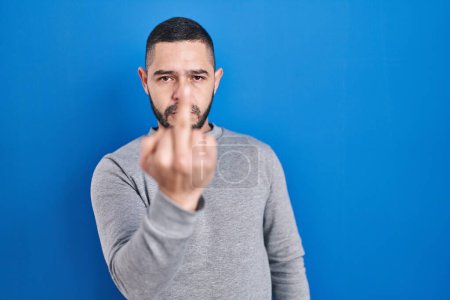 Foto de Hispanic man standing over blue background showing middle finger, impolite and rude fuck off expression - Imagen libre de derechos