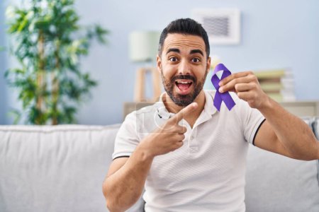 Téléchargez les photos : Jeune homme hispanique avec barbe tenant un ruban violet conscience souriant heureux pointant avec la main et le doigt - en image libre de droit