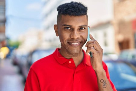 Téléchargez les photos : Jeune homme latino souriant confiant parler sur le smartphone à la rue - en image libre de droit