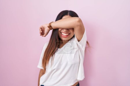 Foto de Mujer árabe joven de pie sobre fondo rosa cubriendo los ojos con el brazo sonriendo alegre y divertido. concepto ciego. - Imagen libre de derechos