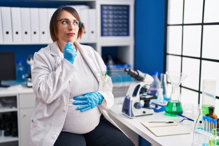 Photo for Pregnant woman working at scientist laboratory thinking worried about a question, concerned and nervous with hand on chin - Royalty Free Image